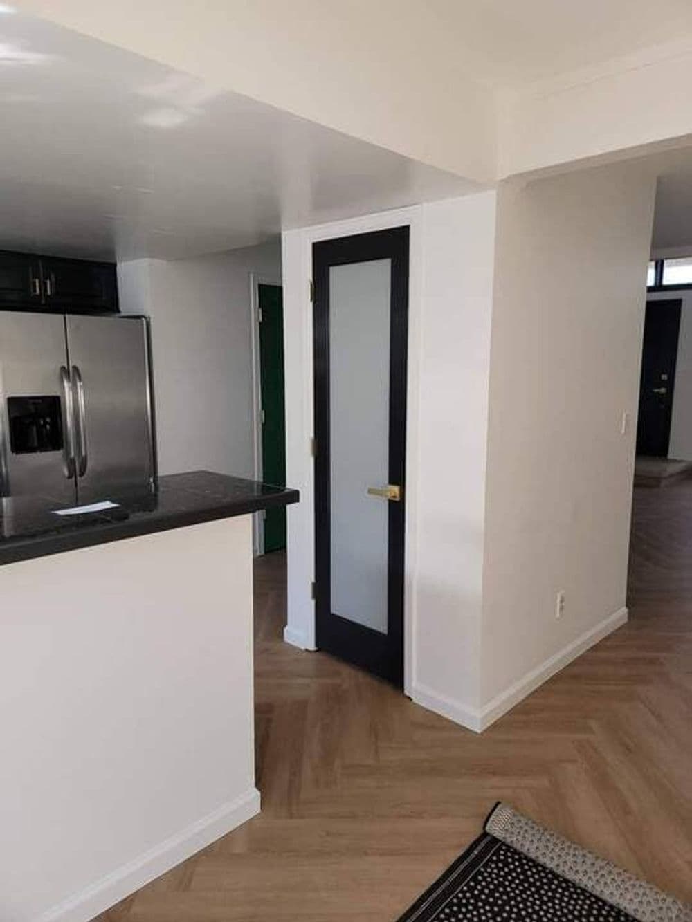 Modern apartment interior featuring black-framed door, open kitchen, and herringbone flooring.