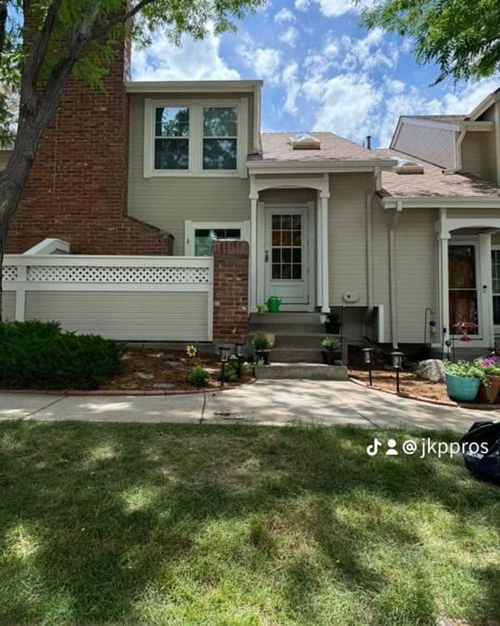 Modern beige house with brick accents, landscaped yard, and sunny sky in the background.