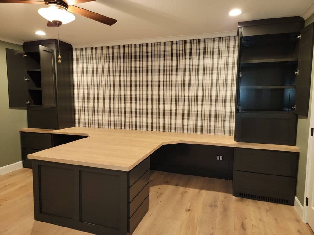 Modern home office with dark cabinetry, a wooden desk, and a plaid accent wall.